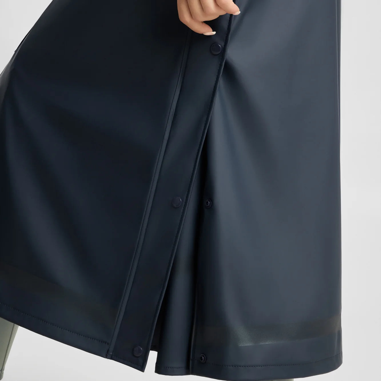 Closeup view of a model wearing the Navy Horze Hazel Womens Long Raincoat on a plain background showing the slits with press buttons