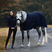 Woman standing next to a horse wearing a blue rug on a road with trees in the background